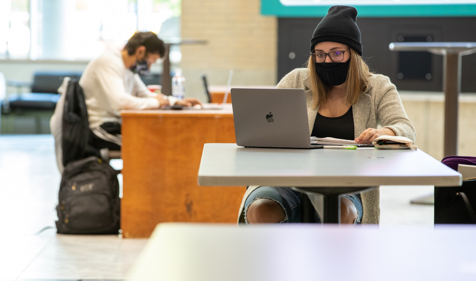 Masked students using computers indoors on campus
