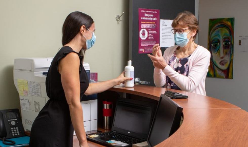 two employees, masked, putting on hand sanitizer